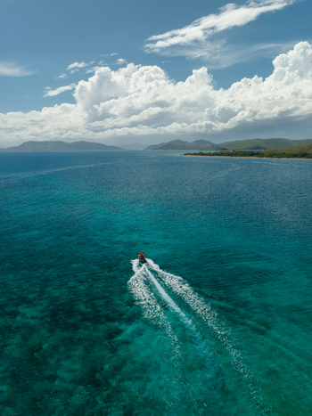 Aerial view of a boat gliding through the turquoise waters leaving a frothy white trail against the backdrop of distant islands Noumea New Caledonia. Aerial view of a boat gliding through the turquoise waters leaving a frothy white trail against the backdrop of distant islands Noumea New Caledonia.