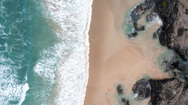 Aerial view of turquoise waves crashing onto the golden sands and dark rocks of Constantine Bay Padstow Cornwall United Kingdom. Aerial view of turquoise waves crashing onto the golden sands and dark rocks of Constantine Bay Padstow Cornwall United Kingdom.