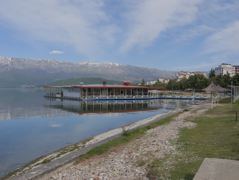View of a floating restaurant on the calm waters of Lake Ohrid with snow capped mountains in the background in Pogradec Korce County Albania. View of a floating restaurant on the calm waters of Lake Ohrid with snow capped mountains in the background in Pogradec Korce County Albania.