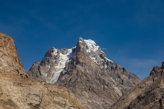 View of Baltoro Glacier featuring rugged snow capped mountain peaks and rocky slopes under a clear blue sky in Baltoro Gilgit Baltistan Pakistan.
