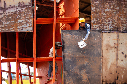 Keraniganj Bangladesh 04 September 2024 View of workers laboring on a large vessel at the Shipyard Dhaka with rusty metal plates and orange scaffolding.