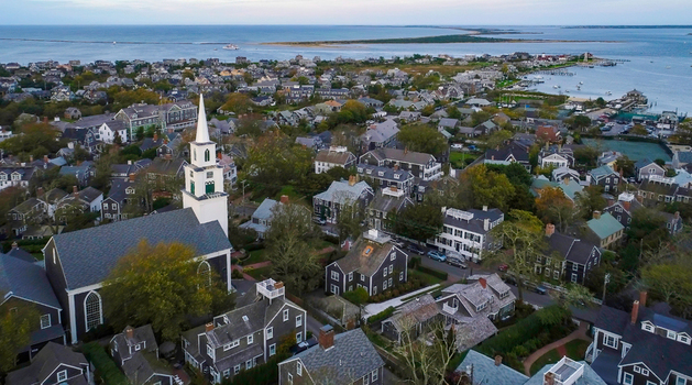View of the historic Nantucket town skyline featuring the white steeple of the First Congregational Church surrounded by traditional shingled houses and the harbor in Nantucket Massachusetts United States.