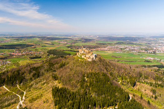 Hechingen Germany 27 September 2026 Aerial view of Hohenzollern Castle perched on a forested hilltop surrounded by rolling green fields and distant towns under a clear blue sky.