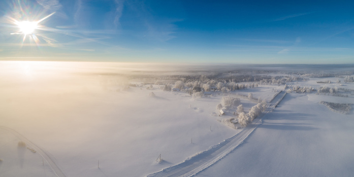 Aerial view of a snow covered landscape with frost covered trees and a road emerging from thick morning fog under a bright sun in Latvia. Aerial view of a snow covered landscape with frost covered trees and a road emerging from thick morning fog under a bright sun in Latvia.