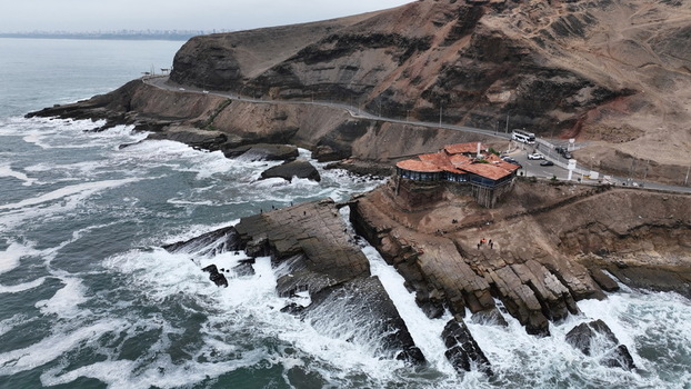 Aerial view of the coastal cliffs and a building in Barranco with waves crashing against the rocky shore along the Pacific Ocean in Barranco Lima Province Peru.