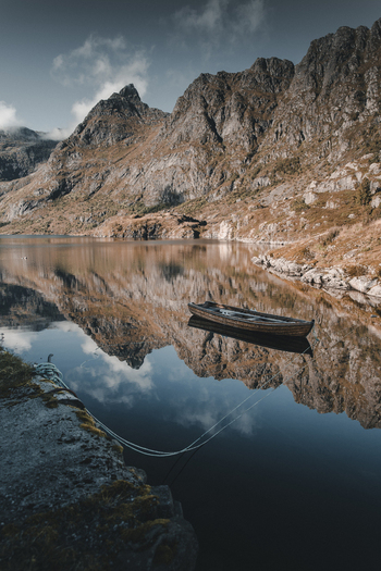 A Nordland Norway 08 September 2022 View of a wooden boat floating on the calm reflective waters of a fjord in the village of A surrounded by rugged mountains.