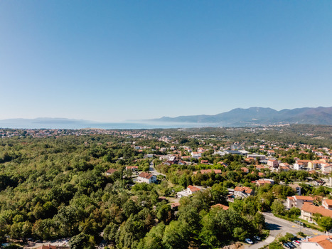 Aerial view of Marcelji town surrounded by lush forests and rolling hills with the Adriatic Sea and distant mountains visible in Marcelji Primorje Gorski Kotar Croatia.