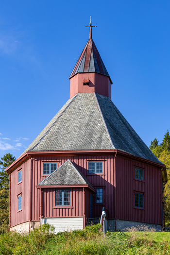 View of the historic red wooden Hadsel Church with its distinctive octagonal shape and shingle roof under a clear blue sky in Stokmarknes Nordland Norway. View of the historic red wooden Hadsel Church with its distinctive octagonal shape and shingle roof under a clear blue sky in Stokmarknes Nordland Norway.