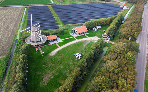 Aerial view of Molen De Hoop windmill surrounded by a large solar panel field green meadows and a small building with a camper van in t Zand North Holland Netherlands. Aerial view of Molen De Hoop windmill surrounded by a large solar panel field green meadows and a small building with a camper van in t Zand North Holland Netherlands.