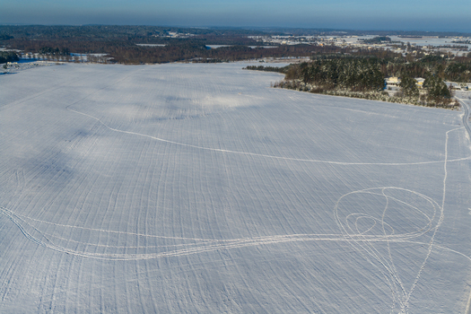 Aerial view of a vast snow covered field with intricate tracks and a distant forest under a clear winter sky in Lithuania. Aerial view of a vast snow covered field with intricate tracks and a distant forest under a clear winter sky in Lithuania.