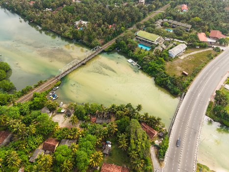 Aerial view of a railway bridge and a road bridge crossing a tropical river surrounded by lush palm trees and coastal buildings in Koggala Southern Province Sri Lanka. Aerial view of a railway bridge and a road bridge crossing a tropical river surrounded by lush palm trees and coastal buildings in Koggala Southern Province Sri Lanka.