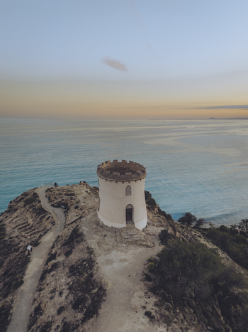 Aerial view of the Santuari iber i roma de la Malladeta tower perched on a rugged cliff overlooking the Mediterranean Sea at sunset in La Vila Joiosa Comunidad Valenciana Spain. Aerial view of the Santuari iber i roma de la Malladeta tower perched on a rugged cliff overlooking the Mediterranean Sea at sunset in La Vila Joiosa Comunidad Valenciana Spain.