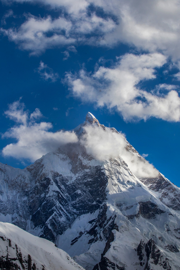 View of the snow capped Masherbrum peak partially covered by clouds under a blue sky in Skardu Gilgit Pakistan.