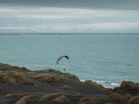 Aerial view of a paraglider soaring above the black sand dunes of Hafnarskeidh with grassy mounds and the sea in the background under a cloudy sky in Sveitarfelagid Olfus Iceland. Aerial view of a paraglider soaring above the black sand dunes of Hafnarskeidh with grassy mounds and the sea in the background under a cloudy sky in Sveitarfelagid Olfus Iceland.