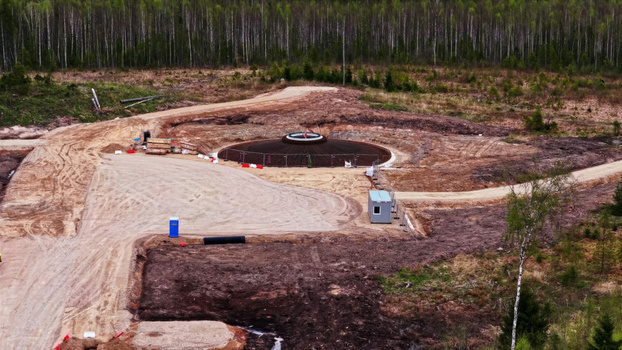 Aerial view of a wind turbine foundation under construction in a forest clearing with dirt access roads and a portable site office in Latvia. Aerial view of a wind turbine foundation under construction in a forest clearing with dirt access roads and a portable site office in Latvia.