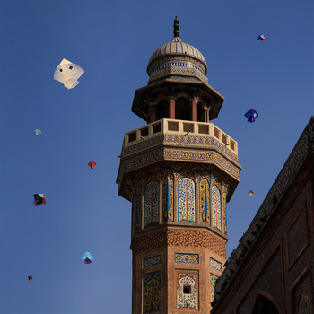View of the ornate minaret of Wazir Khan Mosque with intricate tile work against a clear blue sky filled with colorful kites during the Basant festival Lahore Punjab Pakistan.