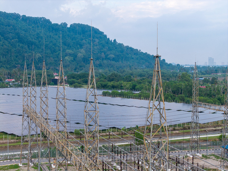 Aerial view of a high voltage transmission substation with steel towers and a large solar panel farm situated against a backdrop of forested hills in Central Seberang Perai Penang Malaysia. Aerial view of a high voltage transmission substation with steel towers and a large solar panel farm situated against a backdrop of forested hills in Central Seberang Perai Penang Malaysia.