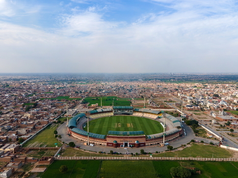 Aerial view of Multan International Cricket Stadium with its green pitch and circular stands surrounded by the urban landscape of Multan Punjab Pakistan.