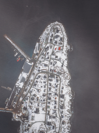 Aerial view of snow blanketed rooftops and the serene harbor contrasting with the dark icy waters surrounding the quaint town Fjordgård Troms Norway. Aerial view of snow blanketed rooftops and the serene harbor contrasting with the dark icy waters surrounding the quaint town Fjordgård Troms Norway.