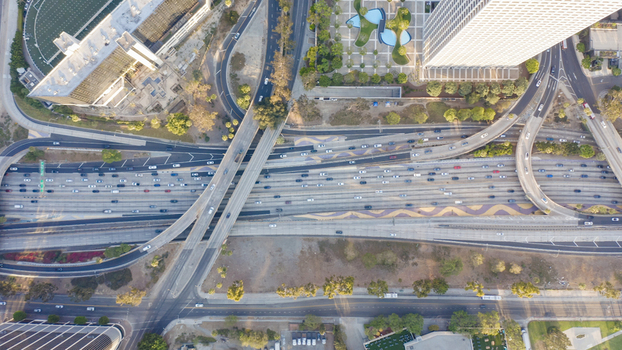 Aerial view of a complex highway interchange with multiple lanes of traffic surrounding urban buildings and landscaped greenery in Los Angeles California United States.