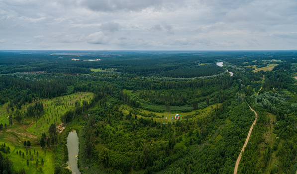 Aerial view of a lush green forest landscape with a winding river and a dirt road under a cloudy sky in Latvia. Aerial view of a lush green forest landscape with a winding river and a dirt road under a cloudy sky in Latvia.