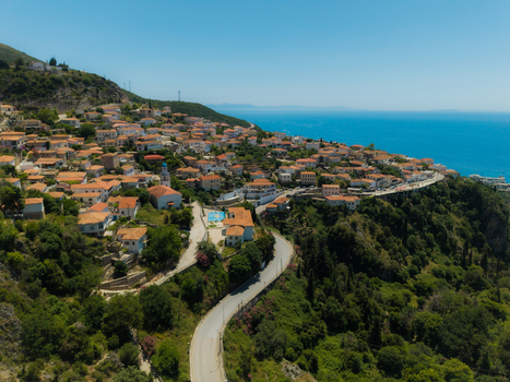 Aerial view of the traditional village of Dhermi with its stone houses and red roofs nestled on a green hillside overlooking the turquoise Ionian Sea Dhermi Vlore County Albania. Aerial view of the traditional village of Dhermi with its stone houses and red roofs nestled on a green hillside overlooking the turquoise Ionian Sea Dhermi Vlore County Albania.