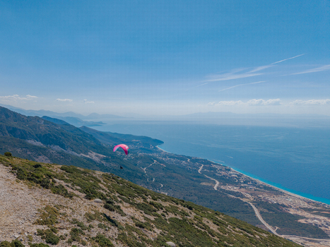 Aerial view of a paraglider soaring above the Llogara Pass with rugged mountains lush green slopes and the turquoise Ionian Sea coastline in Llogara Vlore County Albania. Aerial view of a paraglider soaring above the Llogara Pass with rugged mountains lush green slopes and the turquoise Ionian Sea coastline in Llogara Vlore County Albania.