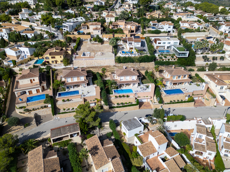 Aerial view of residential villas with swimming pools and terraced gardens in a coastal town featuring Mediterranean architecture and lush greenery in Moraira Valencian Community Spain.