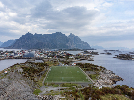 Aerial view of a football field on a small island amidst the vast ocean with a backdrop of majestic mountains Henningsvær Norway. Aerial view of a football field on a small island amidst the vast ocean with a backdrop of majestic mountains Henningsvær Norway.