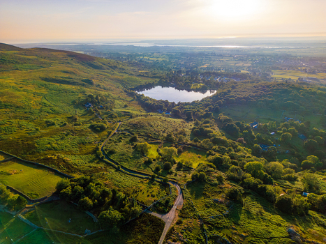 Aerial view of the rolling green hills and stone walls surrounding the reflective waters of the lake near Cwm y glo Wales United Kingdom. Aerial view of the rolling green hills and stone walls surrounding the reflective waters of the lake near Cwm y glo Wales United Kingdom.