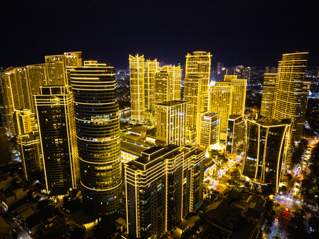 Aerial view of the illuminated skyscrapers of Rockwell Center at night with golden lights outlining the modern architecture in Makati City Metro Manila Philippines.