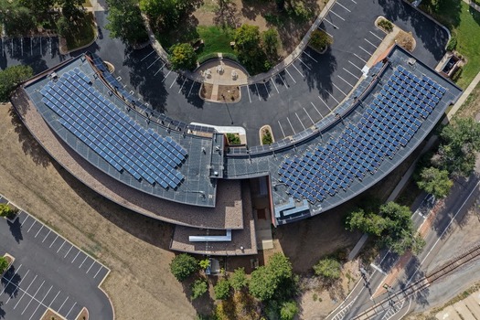 Aerial view of a curved commercial building with extensive rooftop solar panel arrays surrounded by parking lots and mature trees in Boulder Colorado United States. Aerial view of a curved commercial building with extensive rooftop solar panel arrays surrounded by parking lots and mature trees in Boulder Colorado United States.