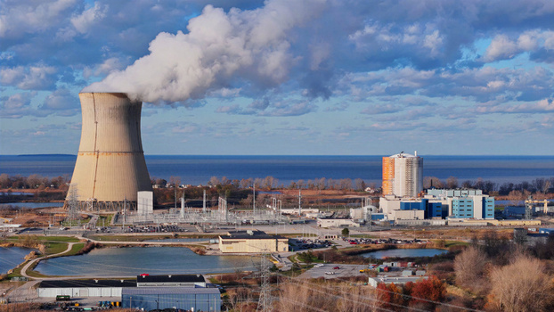Aerial view of Davis Besse Nuclear Power Station with its cooling tower emitting steam power plant buildings and autumn trees along Lake Erie in Oak Harbor Ohio United States.