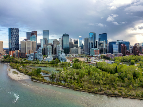 Aerial view of the Calgary skyline rising above the Bow River and lush green parkland under a dramatic cloudy sky Calgary Alberta Canada.