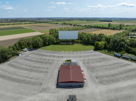 Aerial view of a drive in cinema with a large white screen and empty parking spaces surrounded by green fields and trees in Aschheim Bavaria Germany.