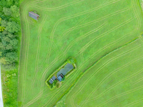 Aerial view of Nationalpark Gesause featuring a small pond surrounded by lush green meadows rustic wooden structures and intricate tire tracks in Admont Steiermark Austria.