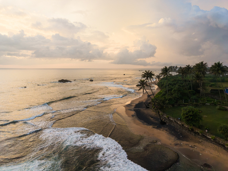 Aerial view of Gintota beach with palm trees lining the sandy shore and waves crashing against the coast under a cloudy sunset sky in Galle Southern Province Sri Lanka. Aerial view of Gintota beach with palm trees lining the sandy shore and waves crashing against the coast under a cloudy sunset sky in Galle Southern Province Sri Lanka.