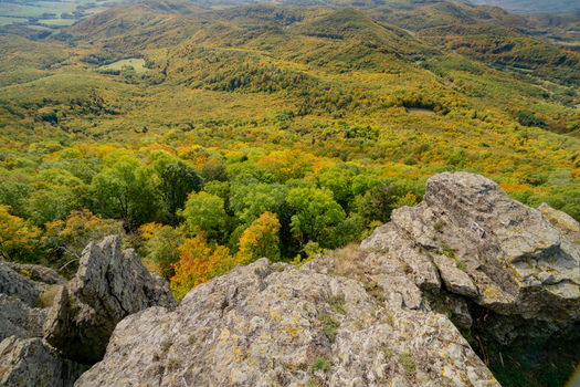 Aerial view of Sitno in Stiavnicke Vrchy featuring rocky cliffs overlooking a vast expanse of dense autumn forest with vibrant foliage in Ilija Banska Bystrica Regio Slovakia.