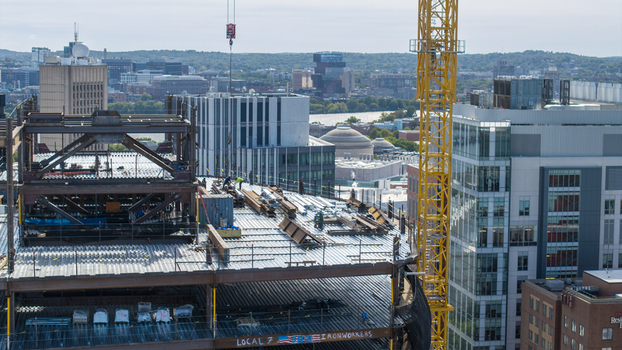 Aerial view of the construction site at Kendall Square featuring steel beams and a tall yellow crane with the urban skyline in Cambridge Massachusetts United States. Aerial view of the construction site at Kendall Square featuring steel beams and a tall yellow crane with the urban skyline in Cambridge Massachusetts United States.