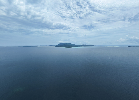 Aerial view of a distant verdant island rising from the tranquil deep blue sea under a soft cloudy sky Karimunjawa Central Java Indonesia.
