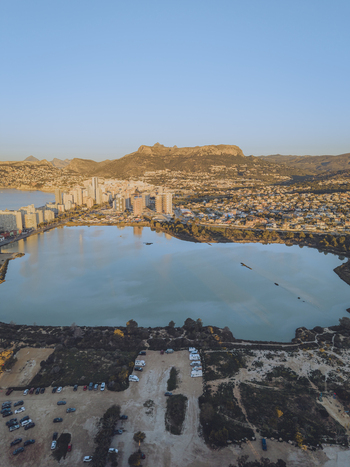 Aerial view of the Las Salinas salt lake surrounded by coastal buildings mountains and a parking area under a clear blue sky Calp Valencian Community Spain. Aerial view of the Las Salinas salt lake surrounded by coastal buildings mountains and a parking area under a clear blue sky Calp Valencian Community Spain.