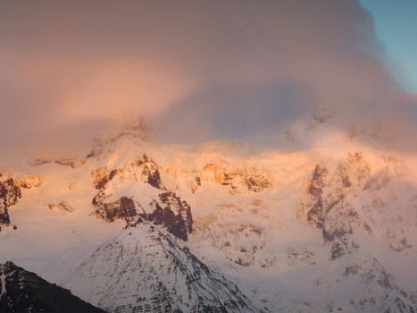 Aerial view of Svinafellsjokull glacier peaks illuminated by warm golden hour light with dramatic clouds clinging to the snow covered mountain ridges in Sveitarfelagid Hornafjordur Iceland. Aerial view of Svinafellsjokull glacier peaks illuminated by warm golden hour light with dramatic clouds clinging to the snow covered mountain ridges in Sveitarfelagid Hornafjordur Iceland.
