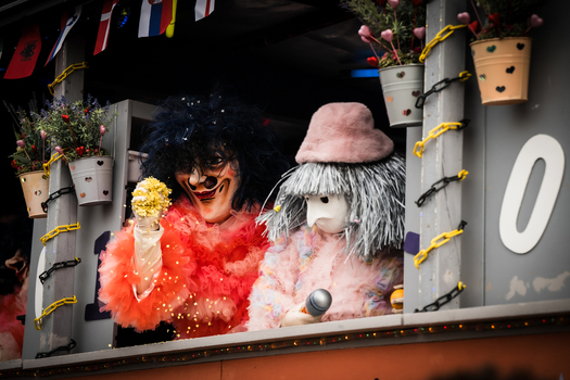 Basel Switzerland 10 March 2025 View of two masked figures in vibrant red and soft pink costumes peering out from a decorated float adorned with flowers and flags. Basel Switzerland 10 March 2025 View of two masked figures in vibrant red and soft pink costumes peering out from a decorated float adorned with flowers and flags.
