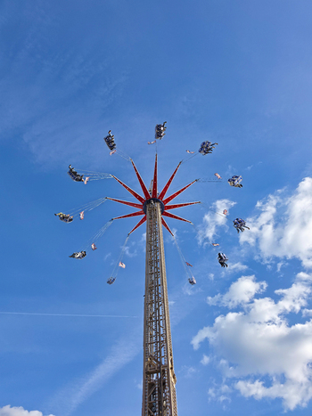 Hanover Lower Saxony Germany 06 April 2026 View of a tall Star Flyer swing ride spinning against a clear blue sky with fluffy white clouds at a fairground.
