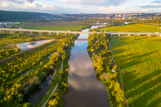 Aerial view of Lahovicky most spanning the Berounka River surrounded by lush green fields trees and a distant cityscape under a golden hour sky in Prague Prague Czechia. Aerial view of Lahovicky most spanning the Berounka River surrounded by lush green fields trees and a distant cityscape under a golden hour sky in Prague Prague Czechia.