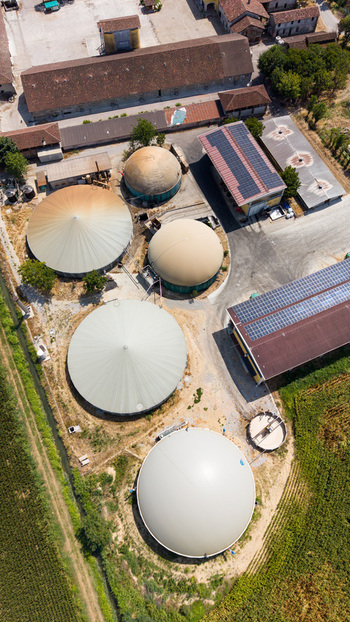 Aerial view of a biomethane production facility featuring large circular digester tanks agricultural buildings with solar panels and surrounding farmland in Tavazzano con Villavesco Lombardy Italy.