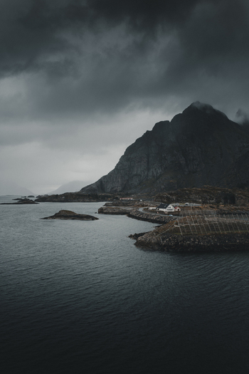 View of Henningsvaer with rocky coastline dark moody sky mountains and calm water in Henningsvaer Nordland Norway. View of Henningsvaer with rocky coastline dark moody sky mountains and calm water in Henningsvaer Nordland Norway.