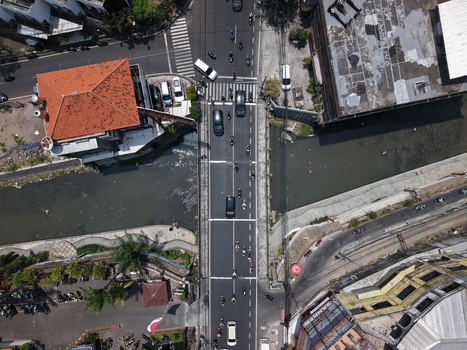 Aerial view of a busy road bridge crossing a river in a dense urban neighborhood with vehicles motorcycles and surrounding buildings in Kecamatan Denpasar Barat Bali Indonesia. Aerial view of a busy road bridge crossing a river in a dense urban neighborhood with vehicles motorcycles and surrounding buildings in Kecamatan Denpasar Barat Bali Indonesia.