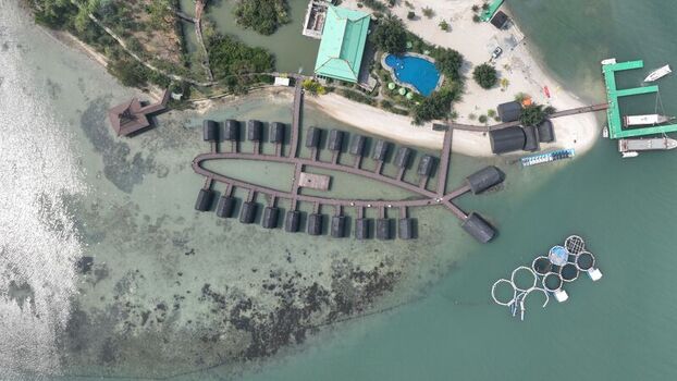 Aerial view of Pulau Lima Resort featuring overwater bungalows in a fish shape connected by wooden walkways with a pool and sandy beach in Kasemen Banten Indonesia. Aerial view of Pulau Lima Resort featuring overwater bungalows in a fish shape connected by wooden walkways with a pool and sandy beach in Kasemen Banten Indonesia.