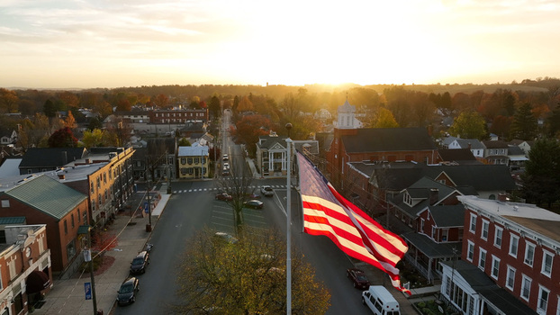 Aerial view of Manheim Square in autumn with vibrant fall foliage historic brick buildings and an American flag waving in the golden sunset light in Manheim Pennsylvania United States. Aerial view of Manheim Square in autumn with vibrant fall foliage historic brick buildings and an American flag waving in the golden sunset light in Manheim Pennsylvania United States.
